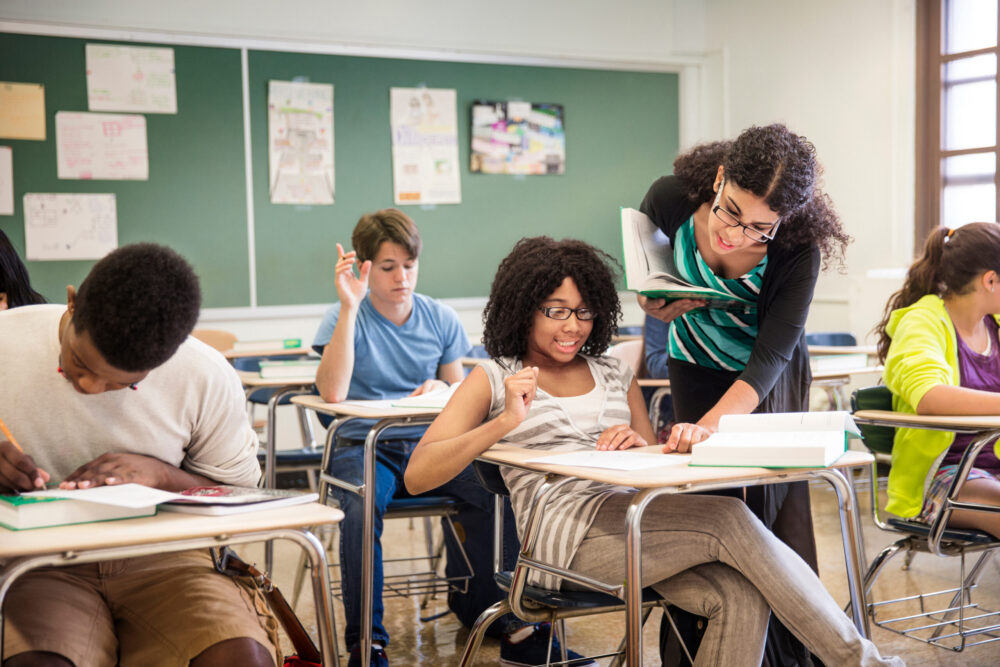 Teacher helping a high school student in a classroom.