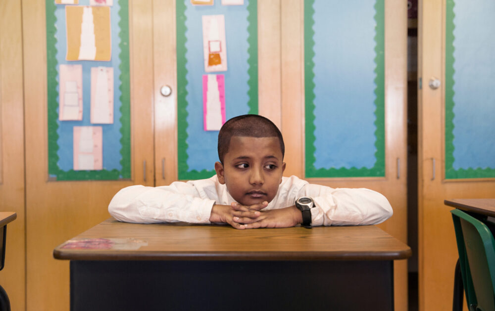 Elementary school student sitting at desk, head on hands.