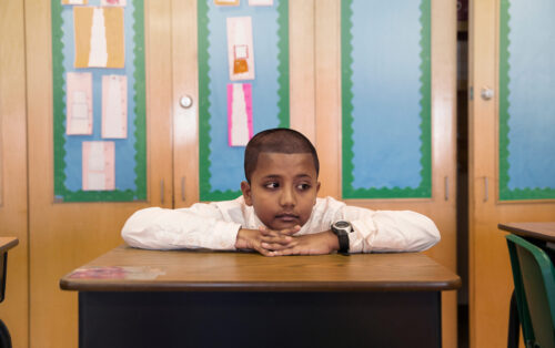 Elementary school student sitting at desk, head on hands.