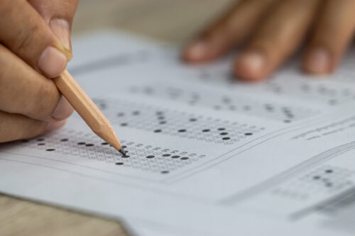 Close-up of a student's hands taking a multiple-choice exam (Photo by smolaw11, Adobe Stock)