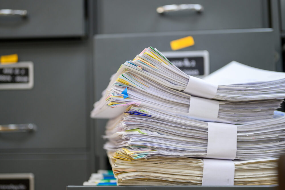 Stack of documents in front of a metal file cabinet.