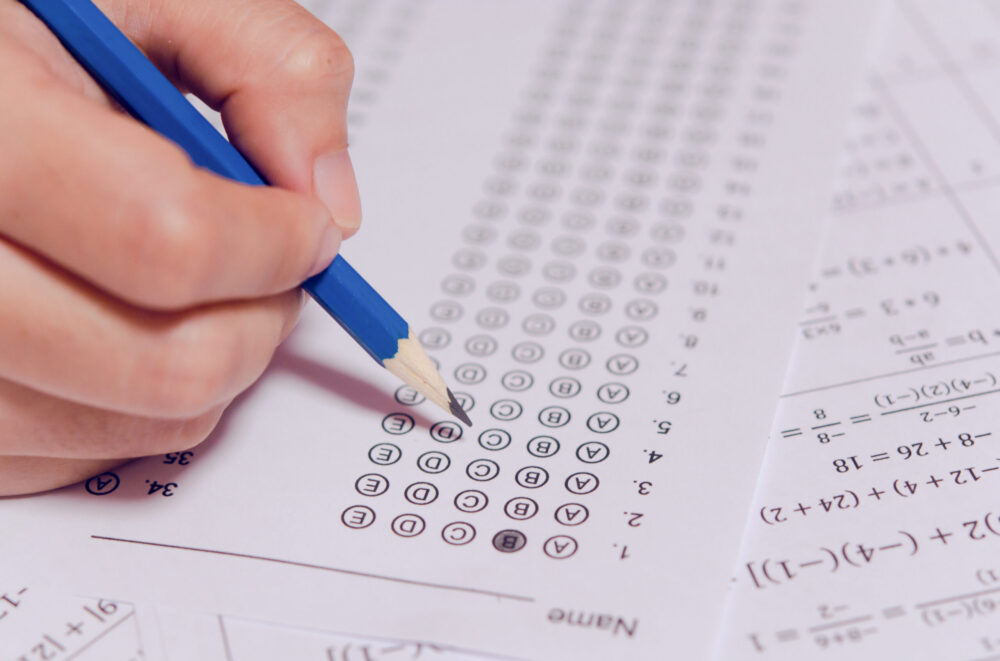 Student's hand holding pencil and filling in a bubble on an answer sheet for a math exam.