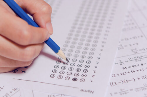 Student's hand holding pencil and filling in a bubble on an answer sheet for a math exam.