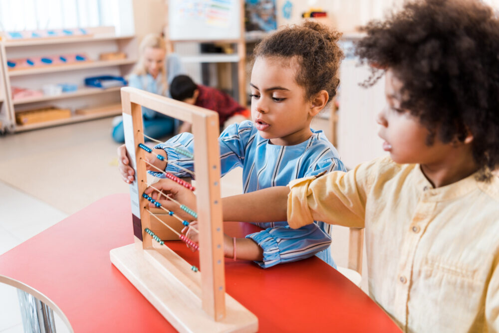 Selective focus of two children playing with scores with teacher and child at background.