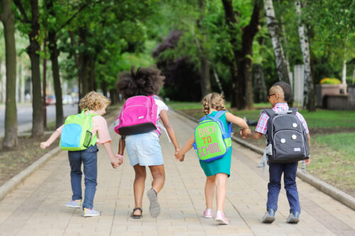 small schoolchildren with colorful school bags and backpacks run to school