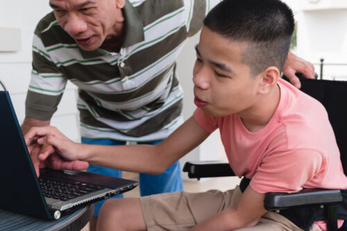 Disabled boy with wheelchair uses laptop computer with his father at home