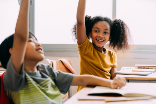 Elementary age students raising hands in class