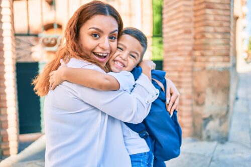 Adorable boy wearing backpack hugging his mom
