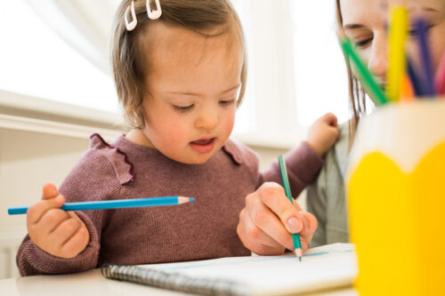 Toddler girl with Down syndrome drawing on a sheet of paper.