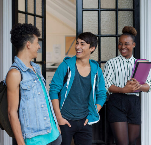 Three teenage students walking out of a school building, laughing