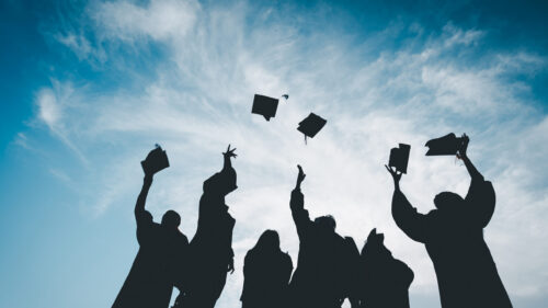 Silhouettes of students throwing mortarboards in the air.