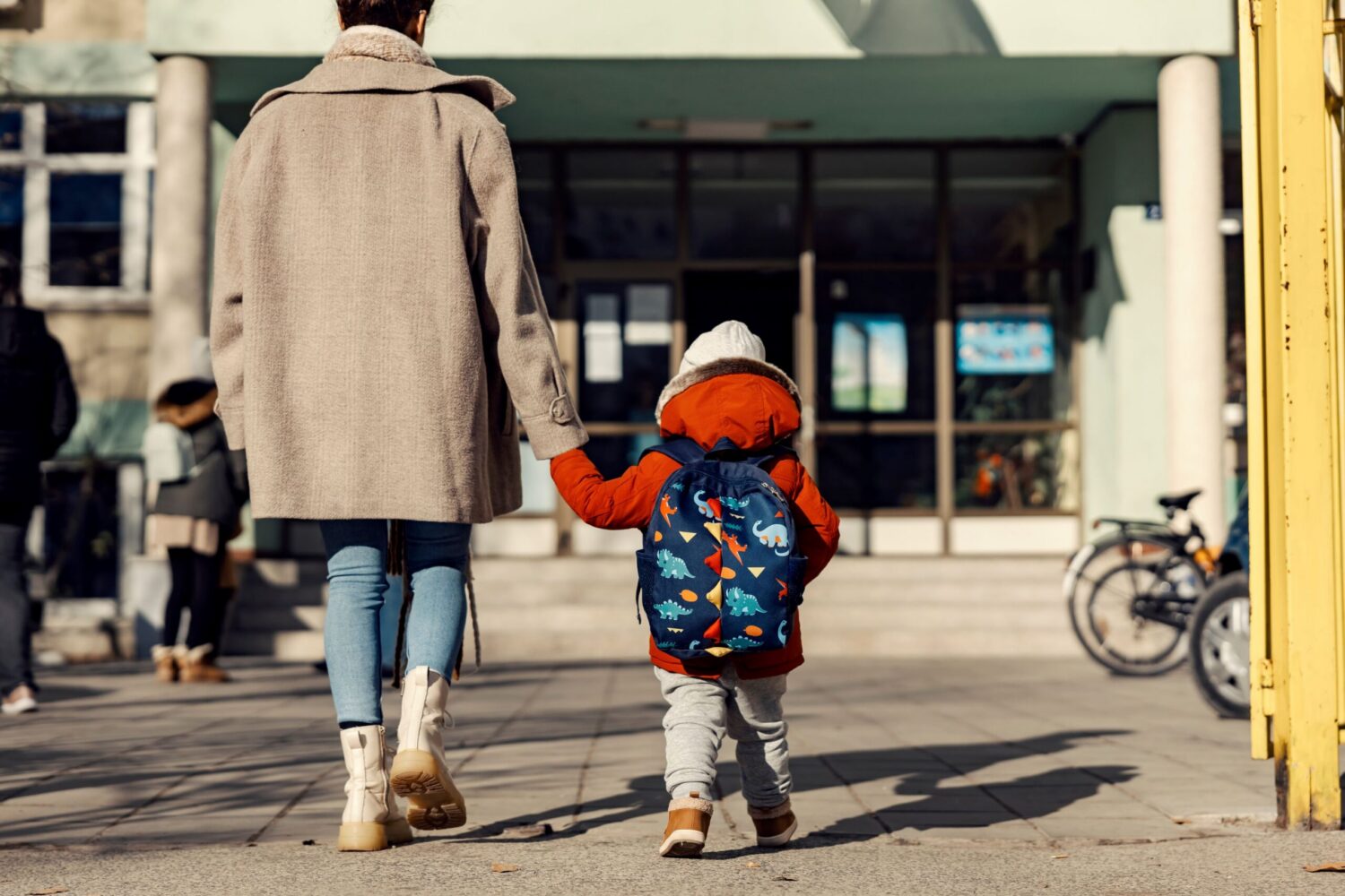 A mother holding hands with her little son and entering a school building