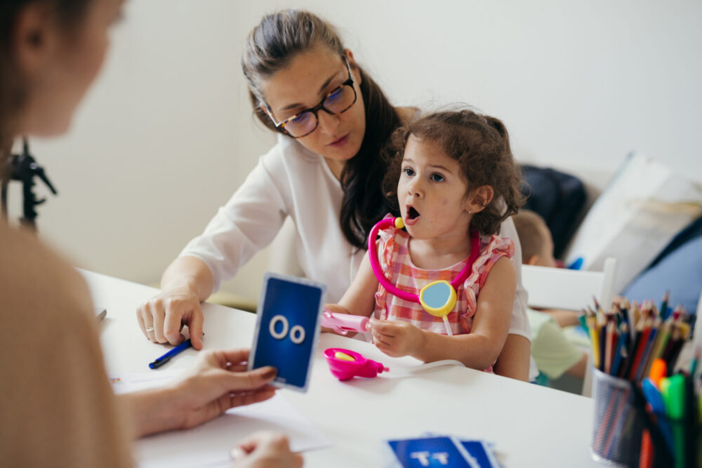 Young child sits on her mother's lap while receiving speech therapy.