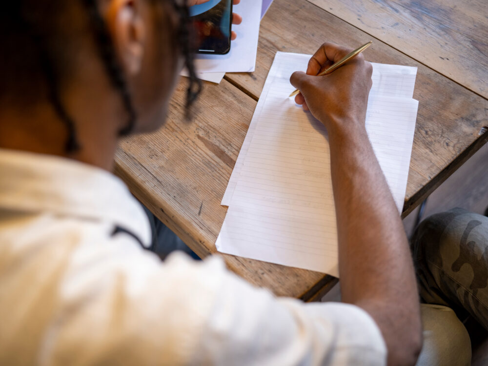 Teenage boy writing, over the shoulder view
