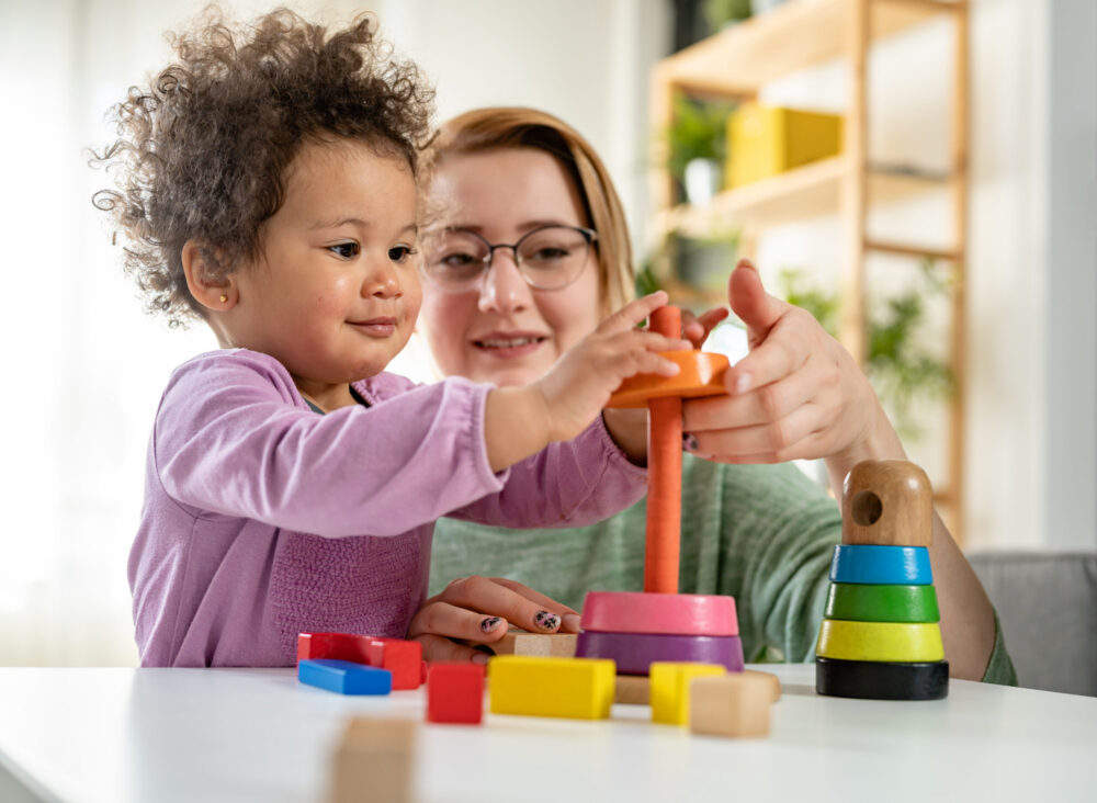 Adult looking at a young child playing with an educational toy.