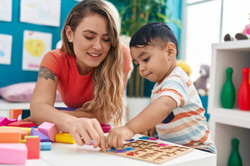 Teacher and toddler sitting at a low table, playing with a math puzzle game