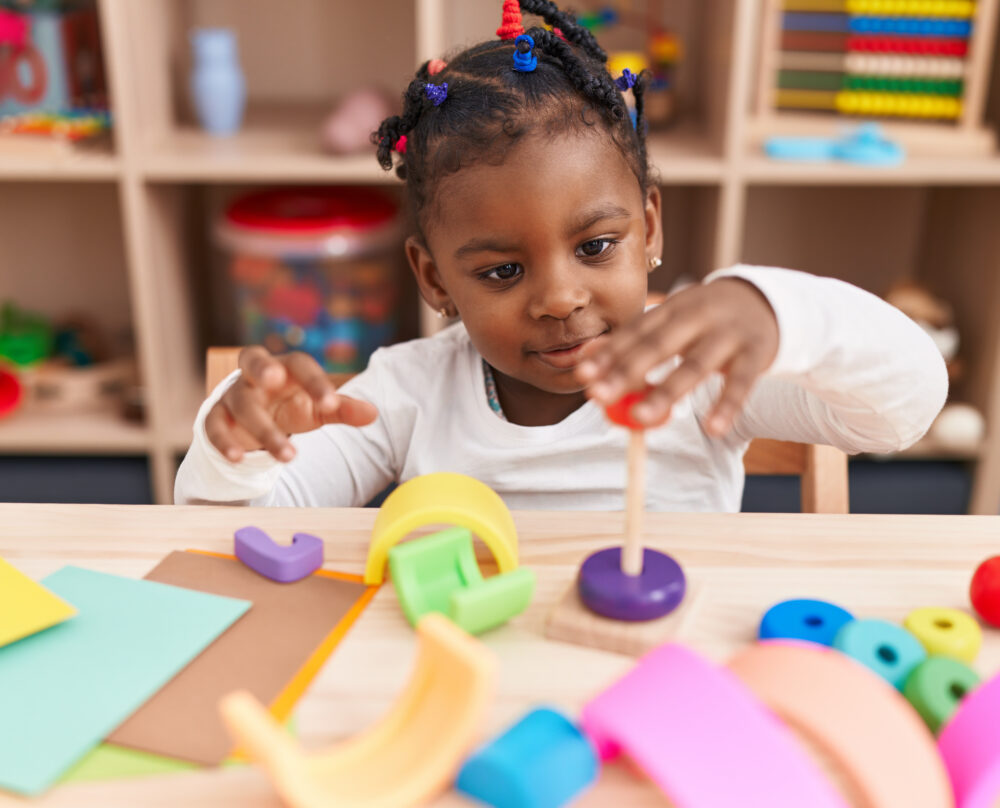 Black preschool girl sitting at table playing with wooden toys