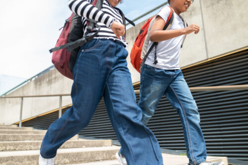 Unidentifiable schoolchildren running on stairs with backpacks wearing casual shirts and jeans. (Photo by zinkevych, Adobe Stock)