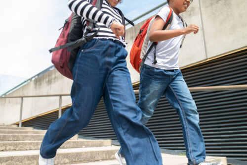 Unidentifiable schoolchildren running on stairs with backpacks wearing casual shirts and jeans.