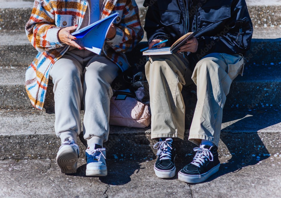 Two teenagers sitting outside doing homework. (Photo by qunica.com, Adobe Stock)