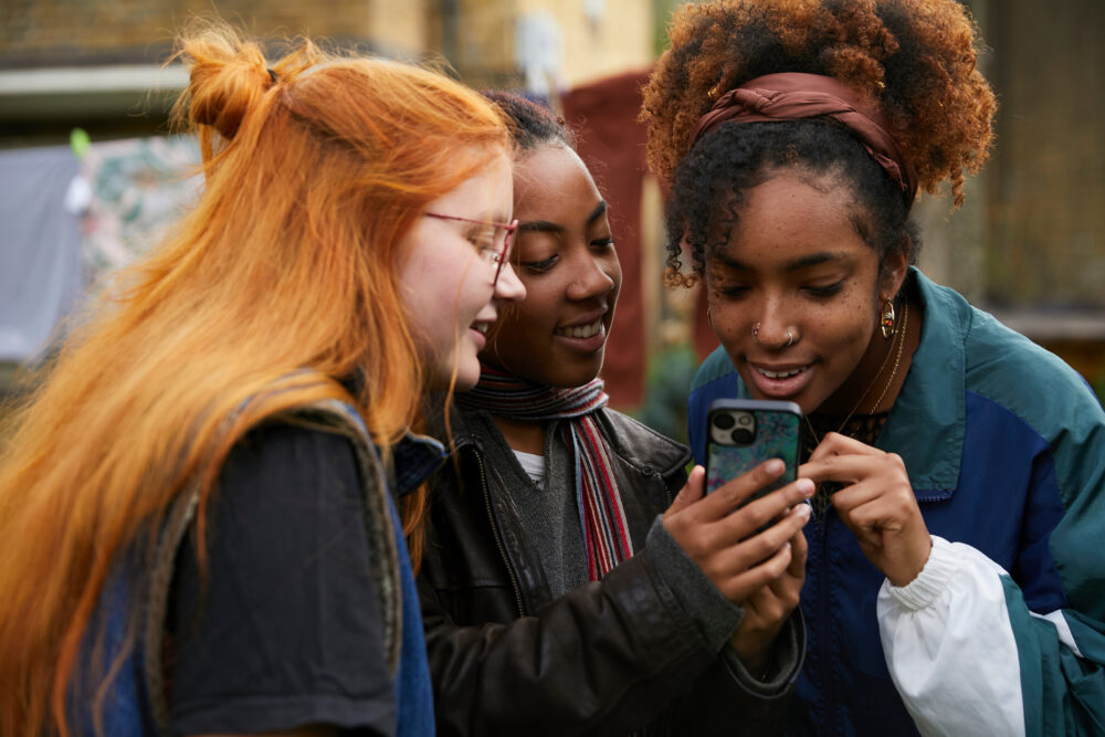 Three teenage girls standing close together, looking at a smartphone
