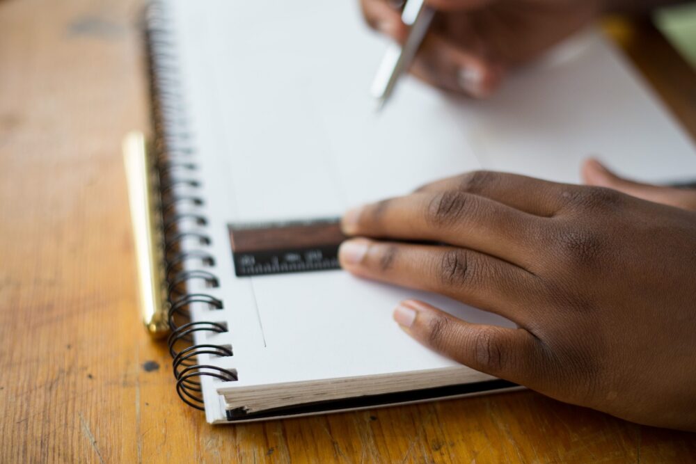 Close-up of hands using a pen and a ruler on a notepad.
