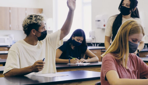 High school teacher and students in a science classroom, wearing protective face masks.