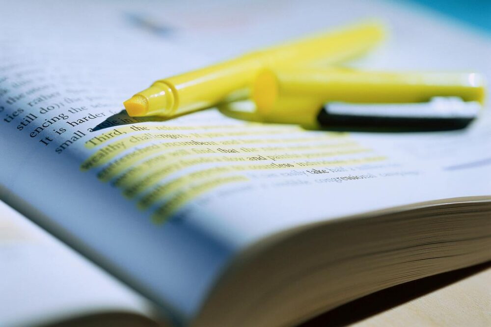 open highlighter lying on top of an open book with a paragraph highlighted
