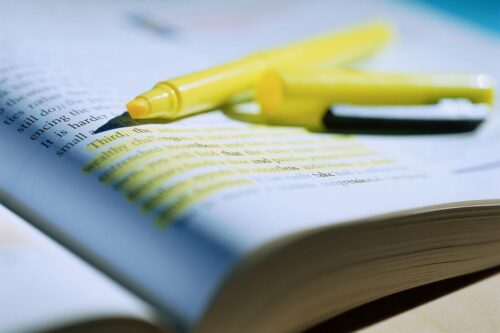 open highlighter lying on top of an open book with a paragraph highlighted
