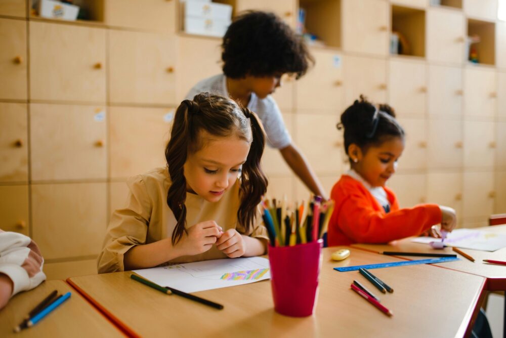 Two young girls drawing in a classroom.
