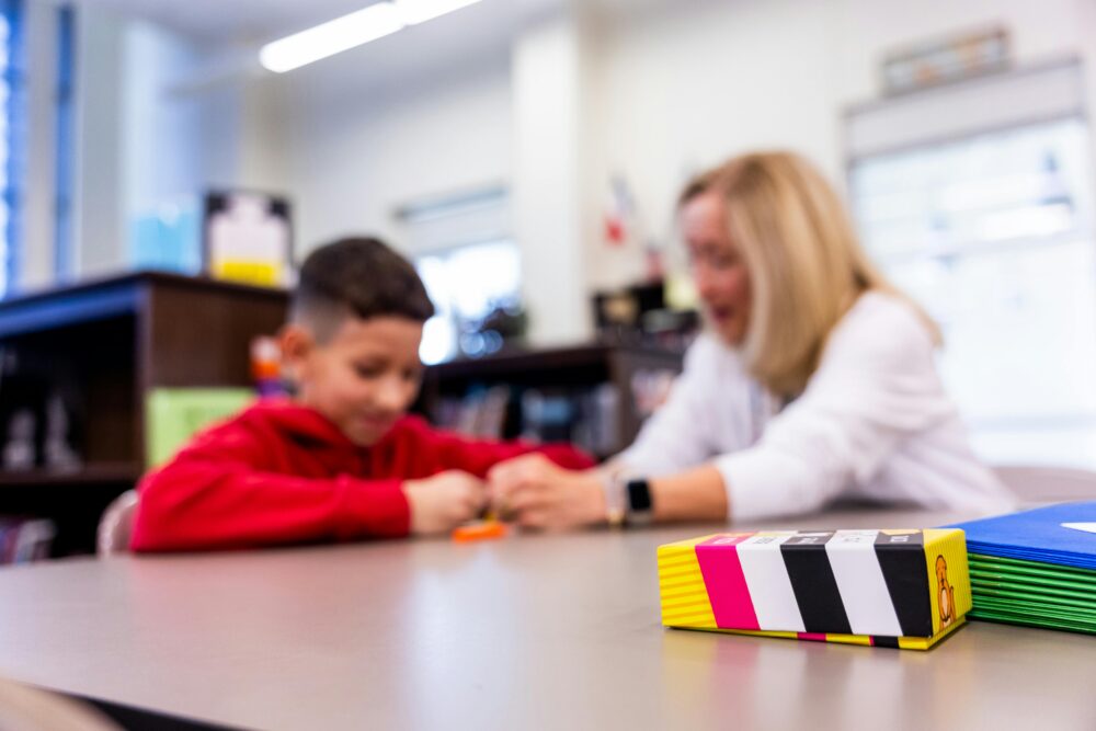 Selective focus of child and teacher at a table in a classroom.