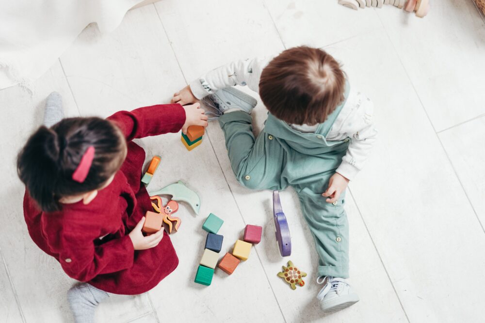 Two preschoolers play with blocks on a wooden floor