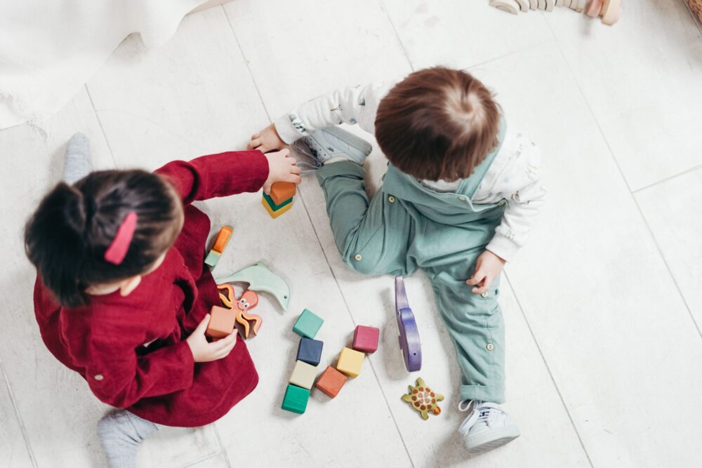 Two preschoolers play with blocks on a wooden floor