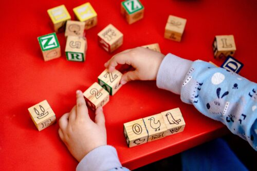 Young child plays with wooden alphabet blocks on a red table.