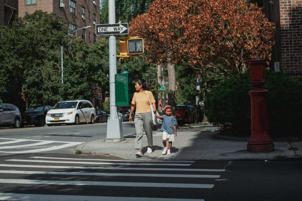 Mother and young child walk across a NYC street.