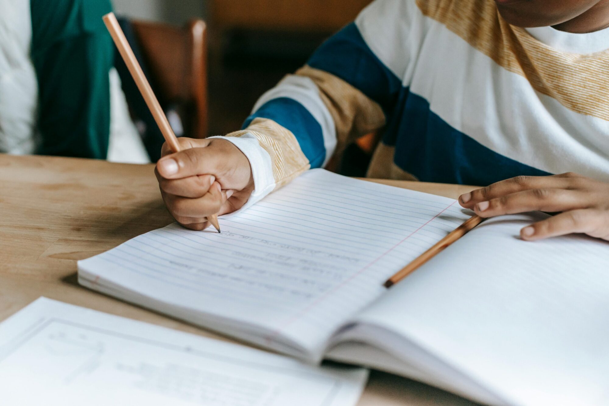 Midsection of Black boy writing in a notebook with a pencil.