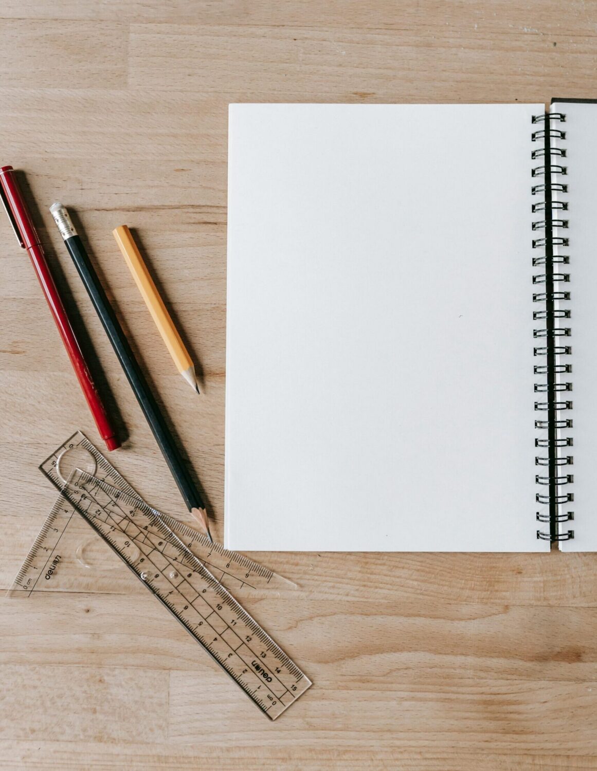 Pencils and rulers lying near an open notebook on a table.