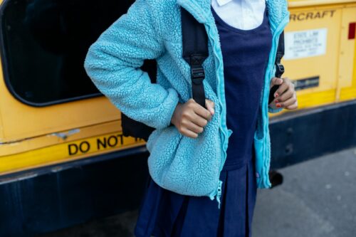 Student in school uniform in front of school bus
