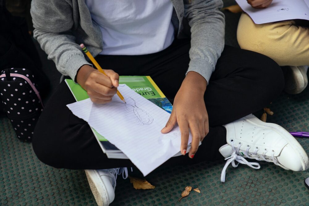 Midsection of a girl sitting on the ground doing schoolwork.