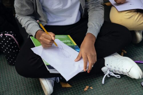 Midsection of a girl sitting on the ground doing schoolwork.