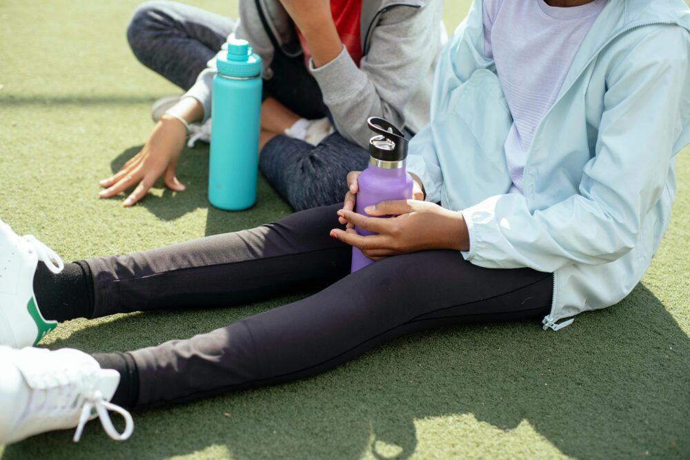 two preteen girls sitting in a school yard with water bottles