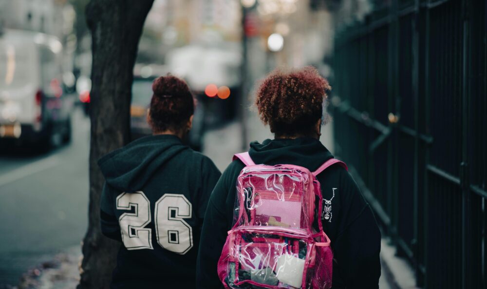 Two teenagers walking down a city street, viewed from behind