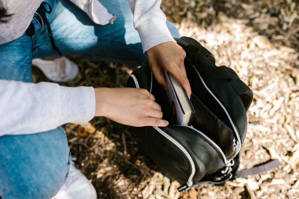 Close-up on kneeling student placing a book in a backpack.