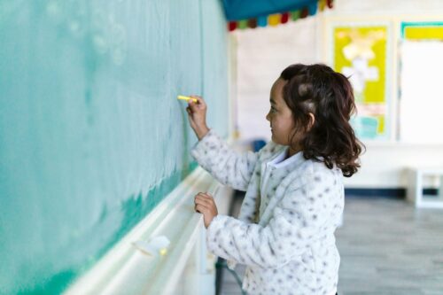 Young girl writes on the chalkboard in a classroom.
