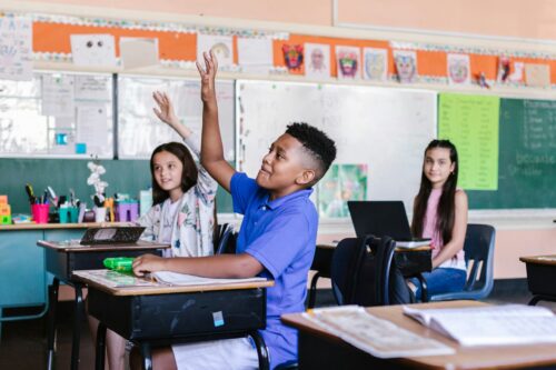 Students raising their hands in a classroom.