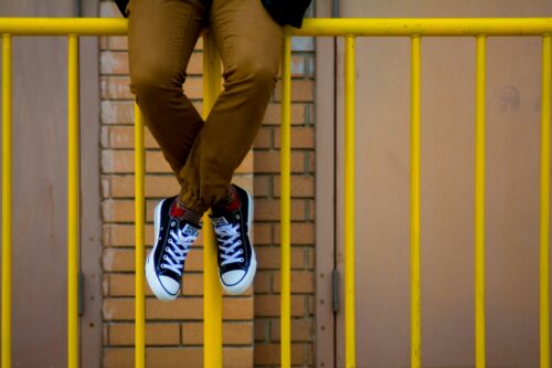 Legs of a teenager sitting on a railing.