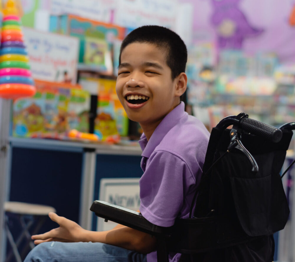 Smiling Asian boy in a wheelchair in a classroom.