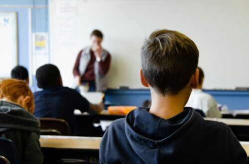 Rear view of a boy wearing black hoodie sitting in a classroom.